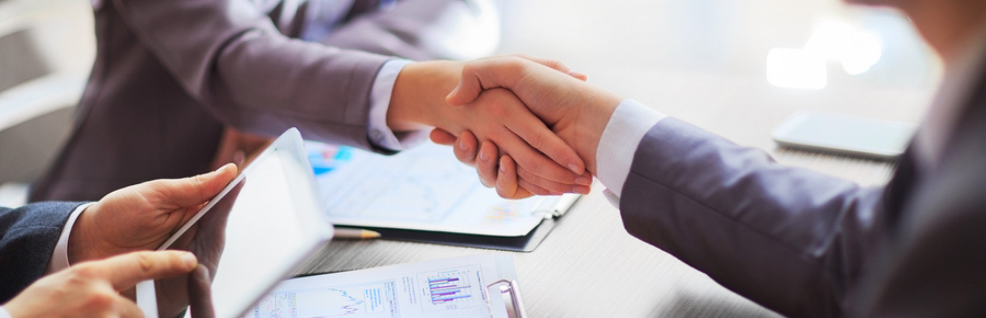 Business partners shaking hands over documents and a tablet at a meeting table