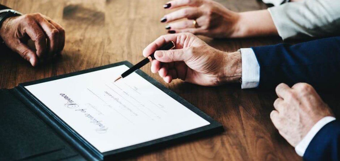 Two people signing a legal document across a desk