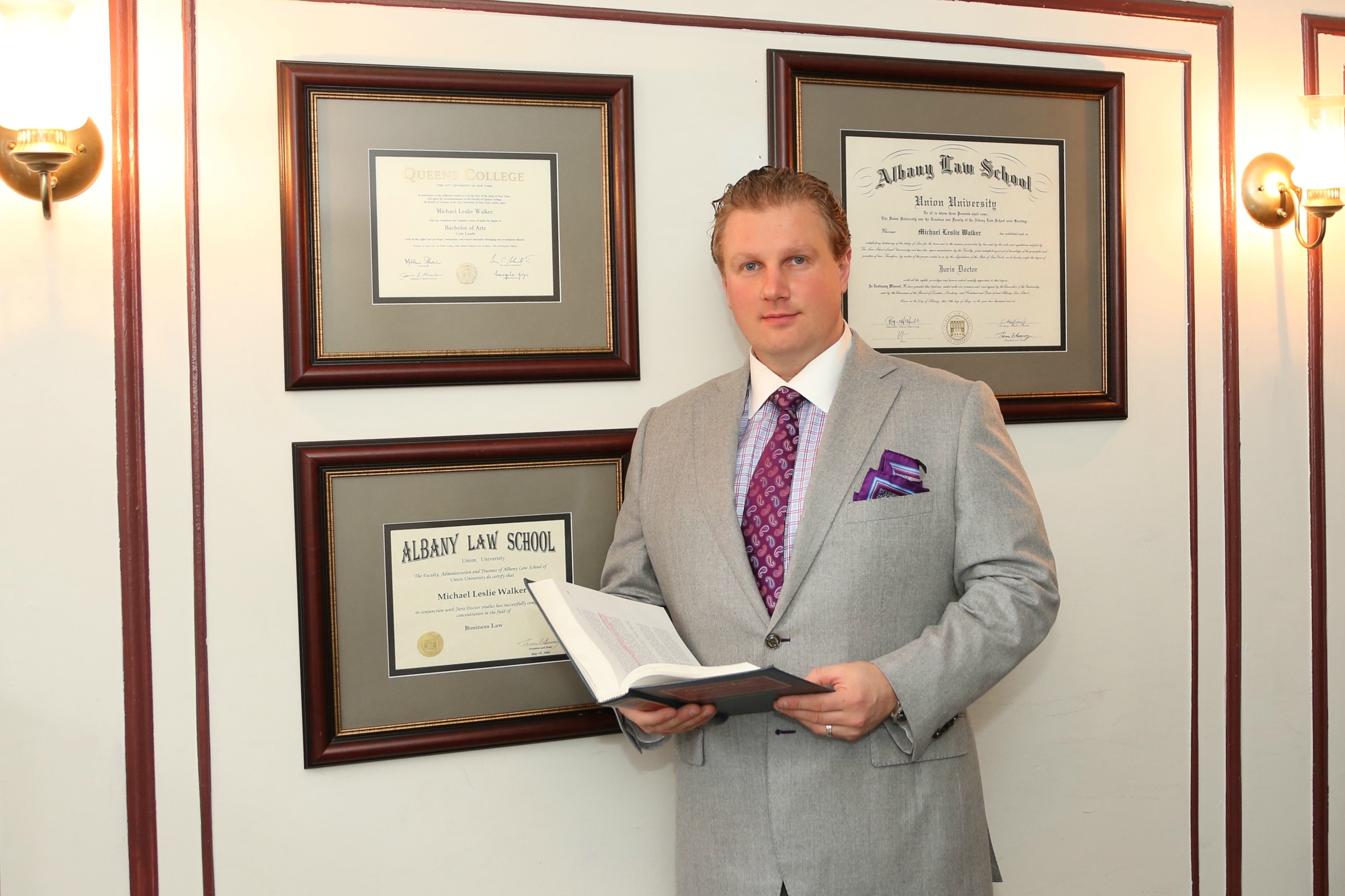 Michael L. Walker standing before his framed law school diploma and bar admission certificates